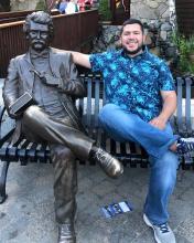 [Photo of Adrian Tamayo sitting next to a statue of Mark Twain on a bench]
